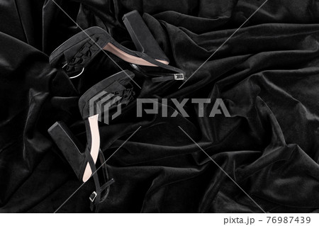 Women's black velvet high-heeled shoes lying on a black fabric, the concept of fashion 76987439
