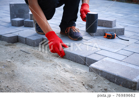The master in yellow gloves lays paving stones The master in yellow gloves lays paving stones 76989662