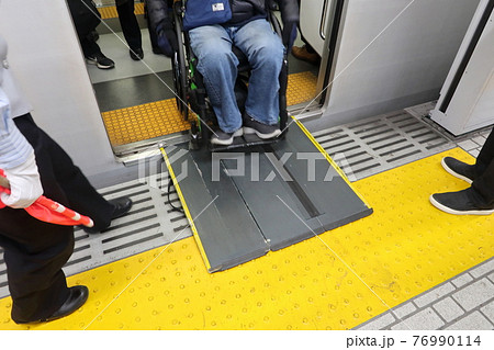 鉄道車両から渡り板を使って降りる車椅子使用者 76990114
