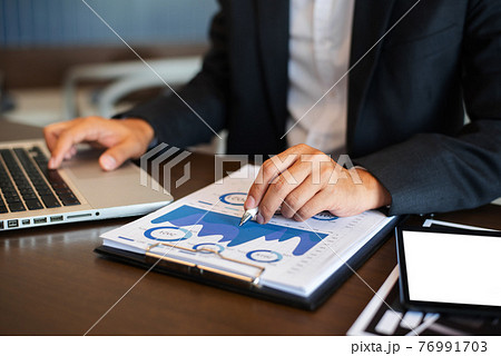 Businessman using digital laptop analyzes business data, busy working on tablet and business report on office desk, business strategy analysis concept. Businessman using digital laptop analyzes business data, busy working on tablet and business report on office desk, business strategy analysis concept. 76991703