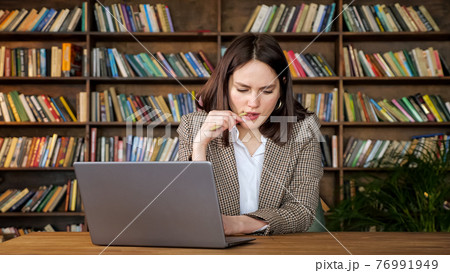 Thoughtful project manager holds pen looking into laptop 76991949