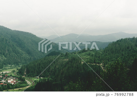 Colorful view from top hill to outskirts city near which winding railway is laid between hills and mountains Colorful view from top hill to outskirts city near which winding railway is laid between hills and mountains 76992788