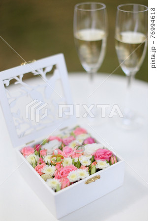Two golden rings lying in flower box near wineglasses with champagne. 76994618