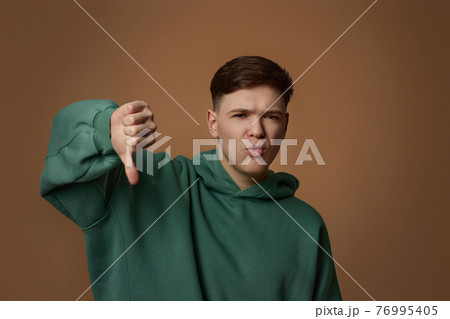 young handsome guy in sweatshirt showing thumb down gesture 76995405