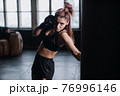 Athletic fit female boxer exercising punches with boxing bag in gym during kickboxing and self defense intensive workout 76996146