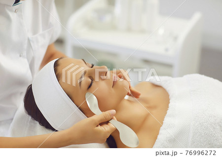 Satisfied woman lies with closed eyes in the masseur's office and receives a facial massage. Satisfied woman lies with closed eyes in the masseur's office and receives a facial massage. 76996272