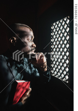 Priest with Bible in confessional Priest with Bible in confessional 76996561