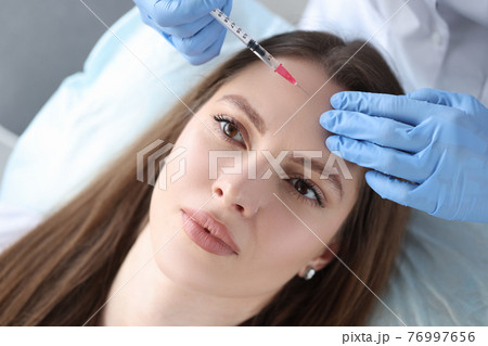 Portrait of woman whose beautician makes injection of botulinum toxin in forehead Portrait of woman whose beautician makes injection of botulinum toxin in forehead 76997656