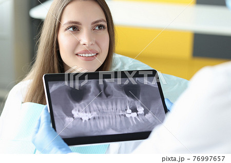 Portrait of smiling woman at dentist appointment holding tablet with an X-ray image of jaw Portrait of smiling woman at dentist appointment holding tablet with an X-ray image of jaw 76997657