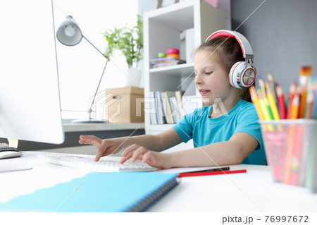 Little girl in headphones in front of computer is typing on keyboard Little girl in headphones in front of computer is typing on keyboard 76997672