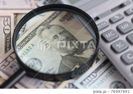On the table are American billsv magnifying glass and calculator. 76997891