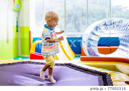 Child jumping on colorful playground trampoline 77003316