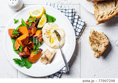 Baked sweet potato slices with spinach and hummus on white plate, top view. 77007298