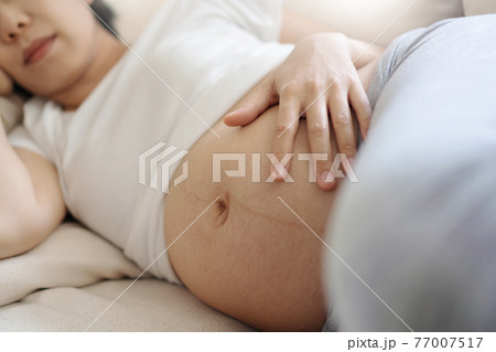 Asian pregnant Woman relaxing lying down and touching belly on sofa. 77007517