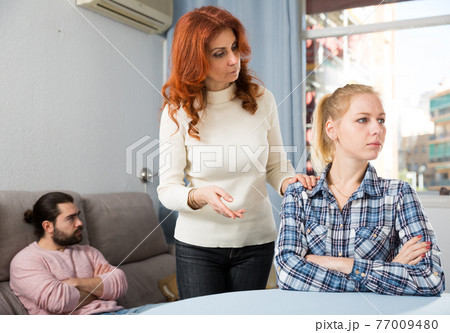 Mature female talking with young daughter at table, man on background 77009480