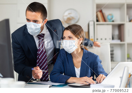 Male and female business partners in masks working in office 77009522