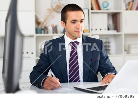 Busy entrepreneur at office desk with papers and laptop Busy entrepreneur at office desk with papers and laptop 77009598