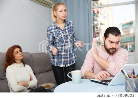 Mom and young wife scolding husband for computer games 77009603