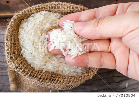 Close up woman hand picking uncooked jasmine rice in small sac on wooden table. Top view. Close up woman hand picking uncooked jasmine rice in small sac on wooden table. Top view. 77010904