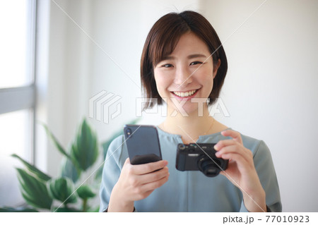 スマートフォンとコンパクトデジタルカメラを持つ女性 77010923