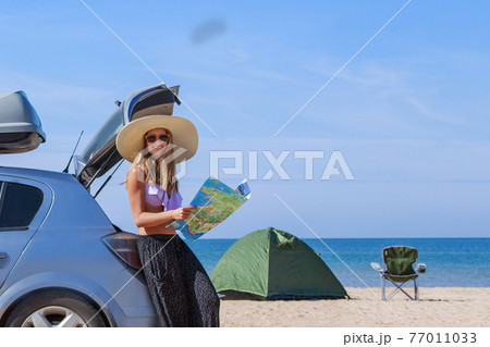 travel to the sea by car. the girl is looking for a road on the map. the car stopped on the beach 77011033