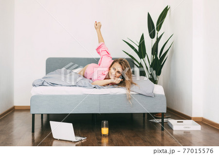 Beautiful blonde woman drinks juice in the morning in bed after waking up and enjoys the weekend Beautiful blonde woman drinks juice in the morning in bed after waking up and enjoys the weekend 77015576