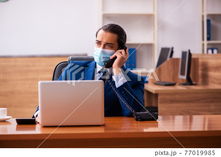 Young male employee working in the office wearing mask 77019985