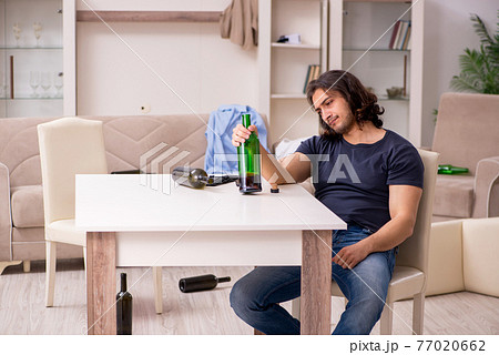 Young unemployed man drinking alcohol at home 77020662