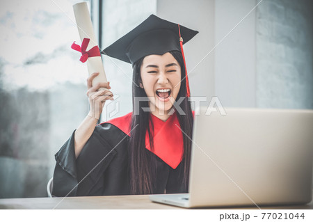 Cute asian smiling graduate holding her diploma and looking happy 77021044
