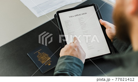 Close up male person getting visa and reading application on tablet, passport on desk. 77021412
