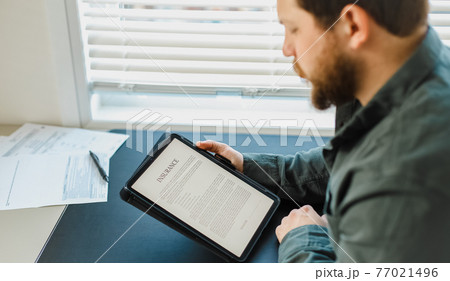 Businessman reading insurance on tablet screen at office. 77021496