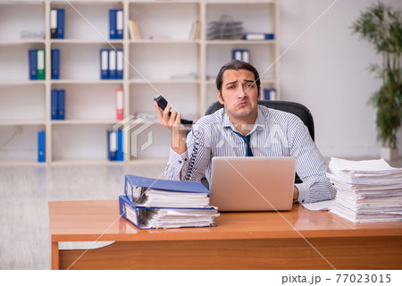 Young male employee unhappy with excessive work in the office Young male employee unhappy with excessive work in the office 77023015