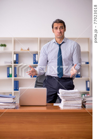 Young male employee unhappy with excessive work in the office 77023018