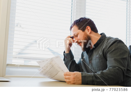 Successful economist reading and filling documents at office near window., 77023586