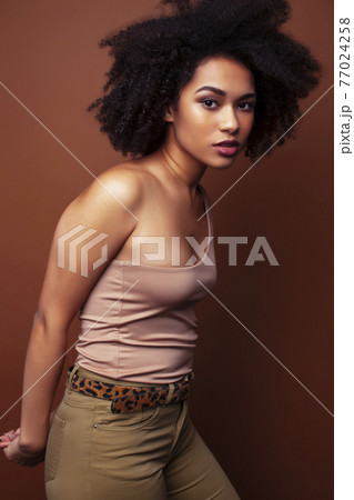 pretty young african american woman with curly hair posing cheerful gesturing on brown background, lifestyle people concept 77024258