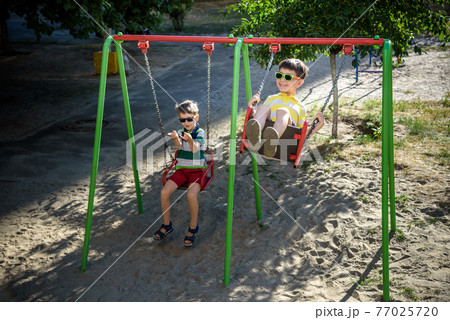 Two little kid boys having fun with swing on outdoor playground. 77025720