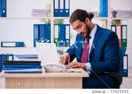 Young male employee and too many work in the office 77025925