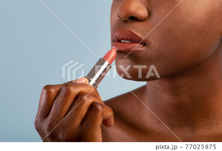 Unrecognizable african american woman using nude lipstick, blue studio background with copy space Unrecognizable african american woman using nude lipstick, blue studio background with copy space 77025975