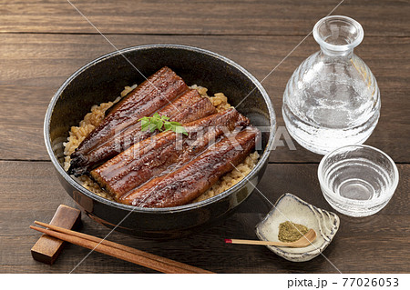 木目のテーブルに置いた黒椀のうな丼と日本酒_木の芽あり 77026053