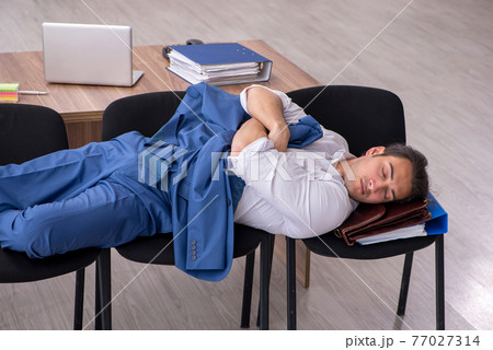 Young male employee sleeping in the office on chairs Young male employee sleeping in the office on chairs 77027314