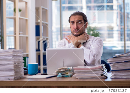 Young male employee unhappy with excessive work in the office Young male employee unhappy with excessive work in the office 77028127