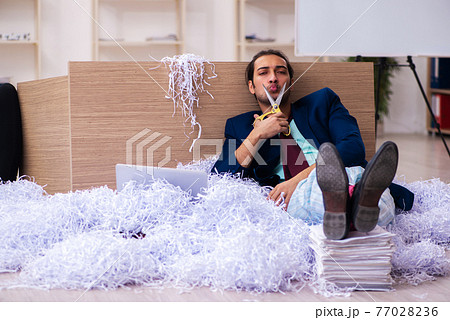 Young male employee and a lot of cut papers in the office 77028236