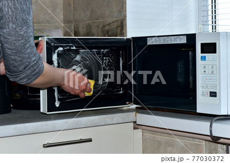 A woman washes the microwave with a washcloth. A woman washes the microwave with a washcloth. 77030372