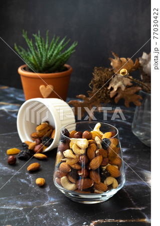 Mix of delicious assorted nuts and dried fruit in white cups on a table, sunny morning. Healthy gourmet vegetarian natural snack. Mix of delicious assorted nuts and dried fruit in white cups on a table, sunny morning. Healthy gourmet vegetarian natural snack. 77030422