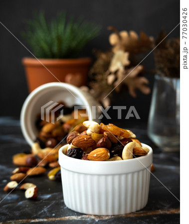 Mix of delicious assorted nuts and dried fruit in white cups on a table, sunny morning. Healthy gourmet vegetarian natural snack. Mix of delicious assorted nuts and dried fruit in white cups on a table, sunny morning. Healthy gourmet vegetarian natural snack. 77030426