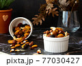 Mix of delicious assorted nuts and dried fruit in white cups on a table, sunny morning. Healthy gourmet vegetarian natural snack. 77030427