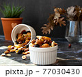 Mix of delicious assorted nuts and dried fruit in white cups on a table, sunny morning. Healthy gourmet vegetarian natural snack. 77030430