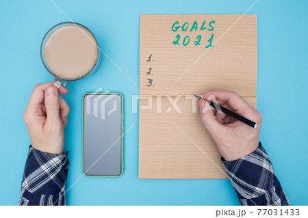 Makes a to do list for the new year 2021 and drinks coffee. Man sets goals for 2021 and write them down in a notebook 77031433
