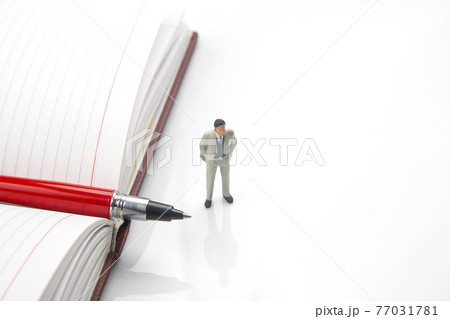 miniature people. figurine of a man on a notebook with a pen. miniature people. figurine of a man on a notebook with a pen. 77031781