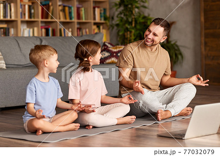 Young cheerful man in casual wear sitting in lotus pose in front of laptop at home Young cheerful man in casual wear sitting in lotus pose in front of laptop at home 77032079